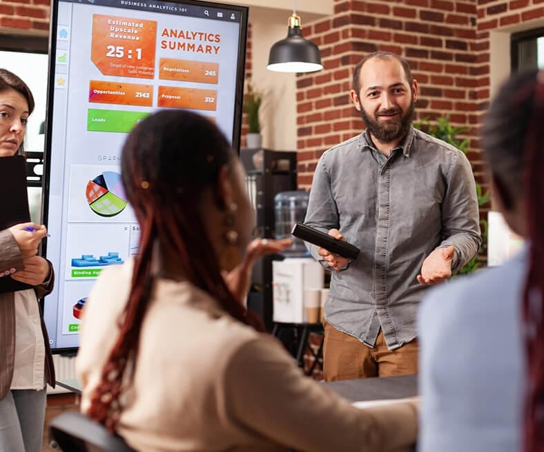 A person presenting an analytics summary on a screen to colleagues in an office.