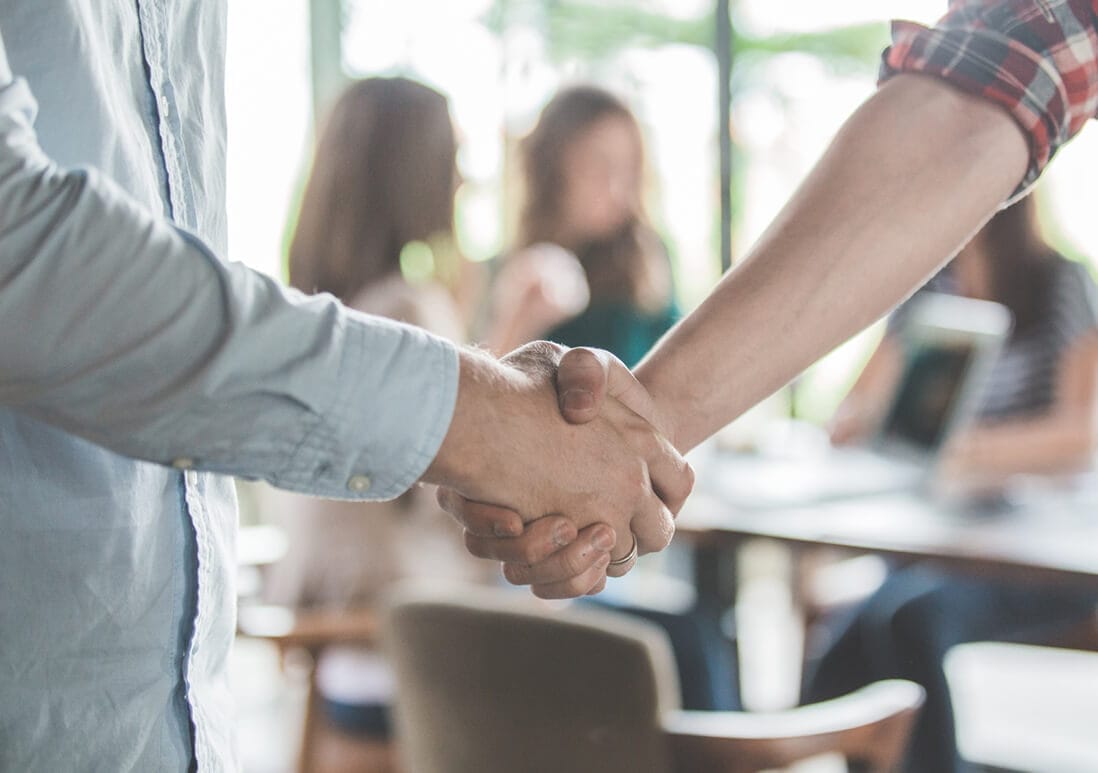 Two people shaking hands in a cafe setting.