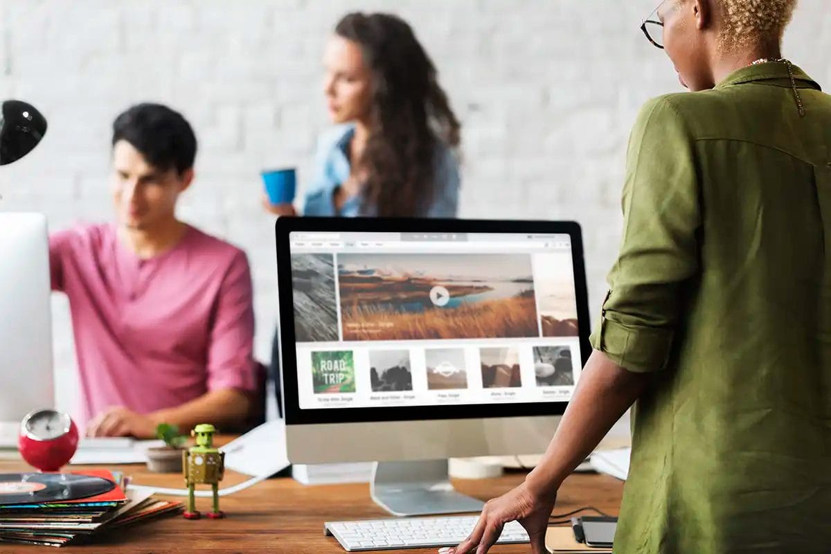a group of creative professionals web design working in an office, with one person using a desktop computer displaying media content, indicating a creative workspace or digital media project