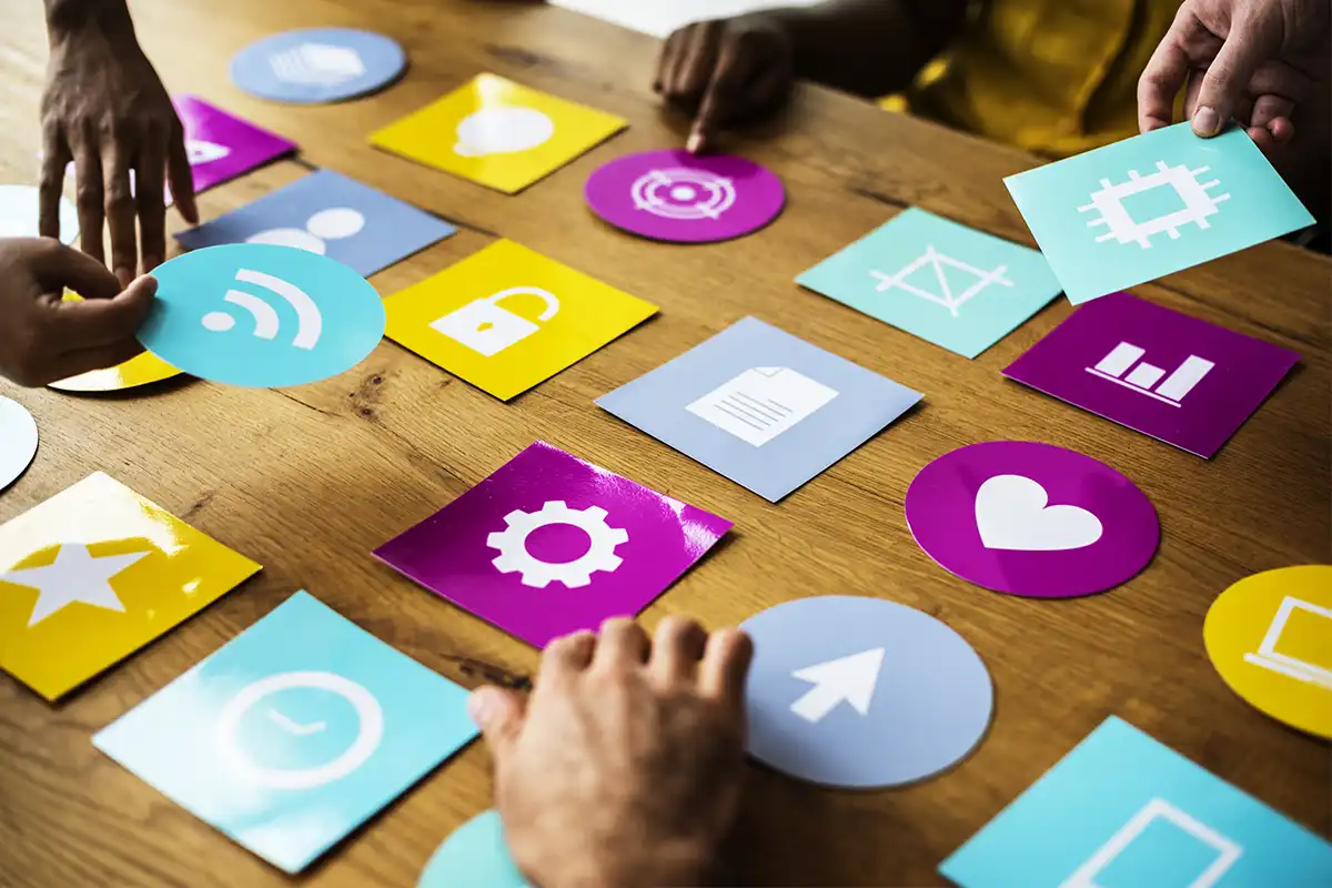 a group of people arranging colorful icon cards on a wooden table, representing social media marketing agency las vegas