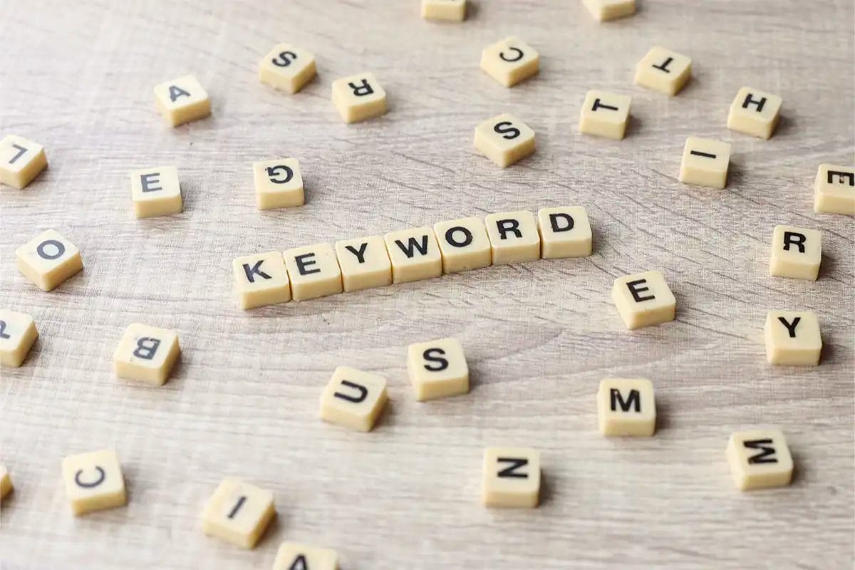 beige letter tiles on a wooden surface with the word ‘keyword’ spelled out in the center, surrounded by scattered random letters, symbolizing google ad services keyword optimization