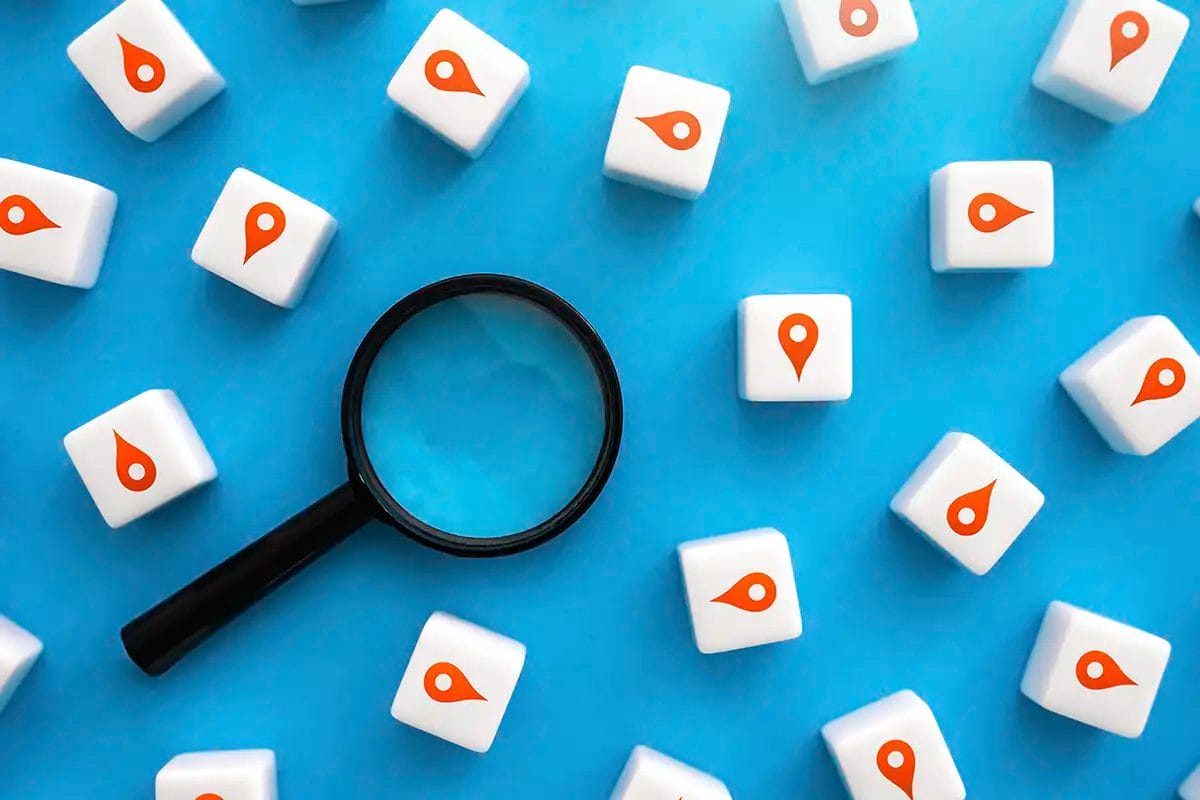 black magnifying glass surrounded by white cubes with orange location pin icons on a blue background, representing local seo services