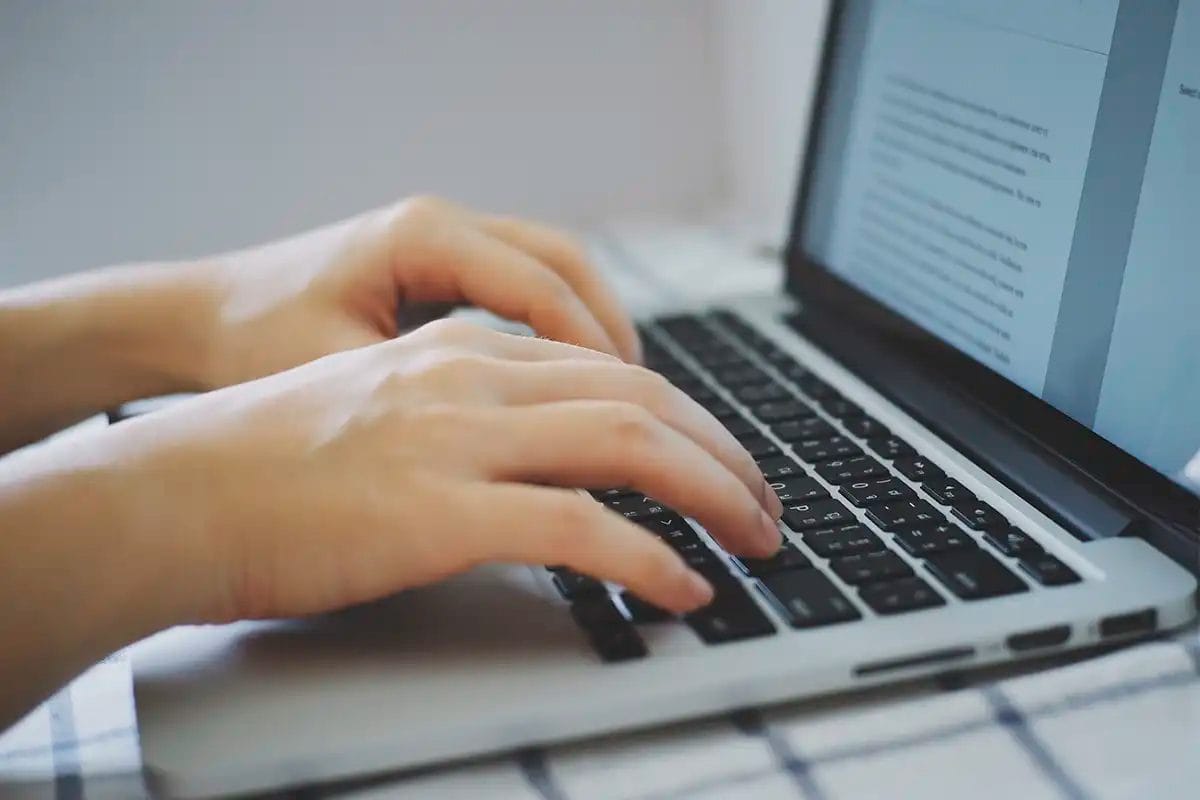 close up of hands typing on a laptop keyboard with a document open on the screen, representing writing and editing for on page seo services