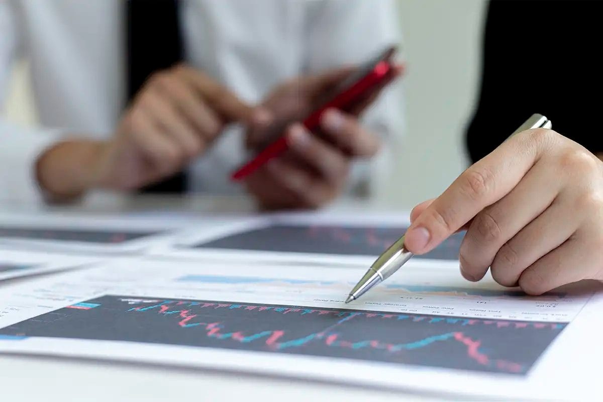 close up of two people reviewing printed charts with graphs; one hand points with a pen, while the other person holds a red smartphone in the background symbolizing local seo services