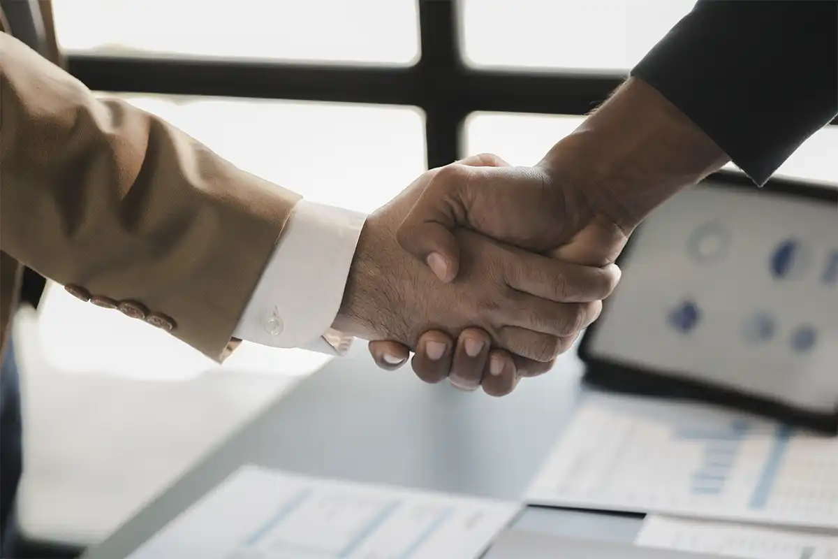 close up of two people shaking hands across a desk with business documents and charts, representing a professional agreement with on page seo services