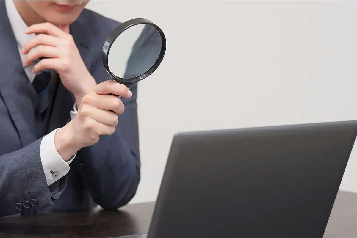 person in a suit holding a magnifying glass in front of a laptop, with a thoughtful pose, symbolizing technical seo services