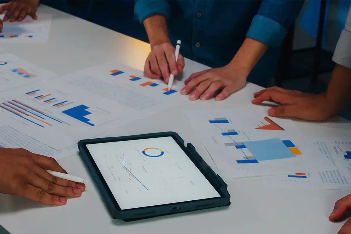 team members collaborating at a table, reviewing printed charts and digital tablet graphs with colorful bar, line, and pie charts during a data analysis for on page seo services