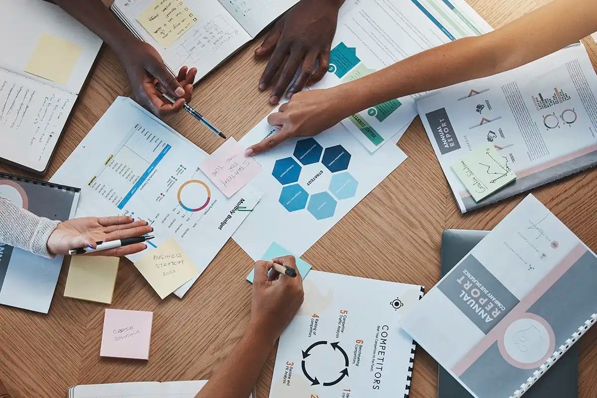 top down view of a collaborative business meeting with multiple hands working over charts and reports, on a wooden table, symbolizing strategy planning for social media advertising services