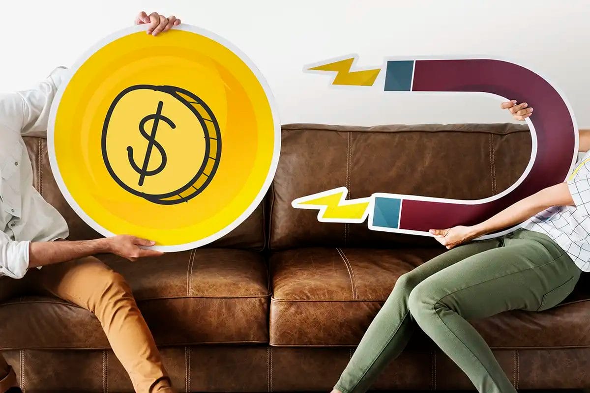 two people sitting on a couch holding oversized cutouts of a dollar coin and a horseshoe magnet, symbolizing social media advertising services