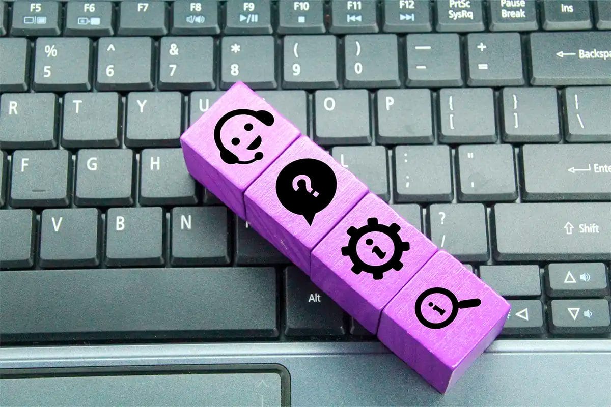 four wooden blocks with icons customer support headset, question mark in a speech bubble, gear with information symbol, and magnifying glass with info)resting on a black computer keyboard. The image symbolizes Q&A monitoring for google maps services.